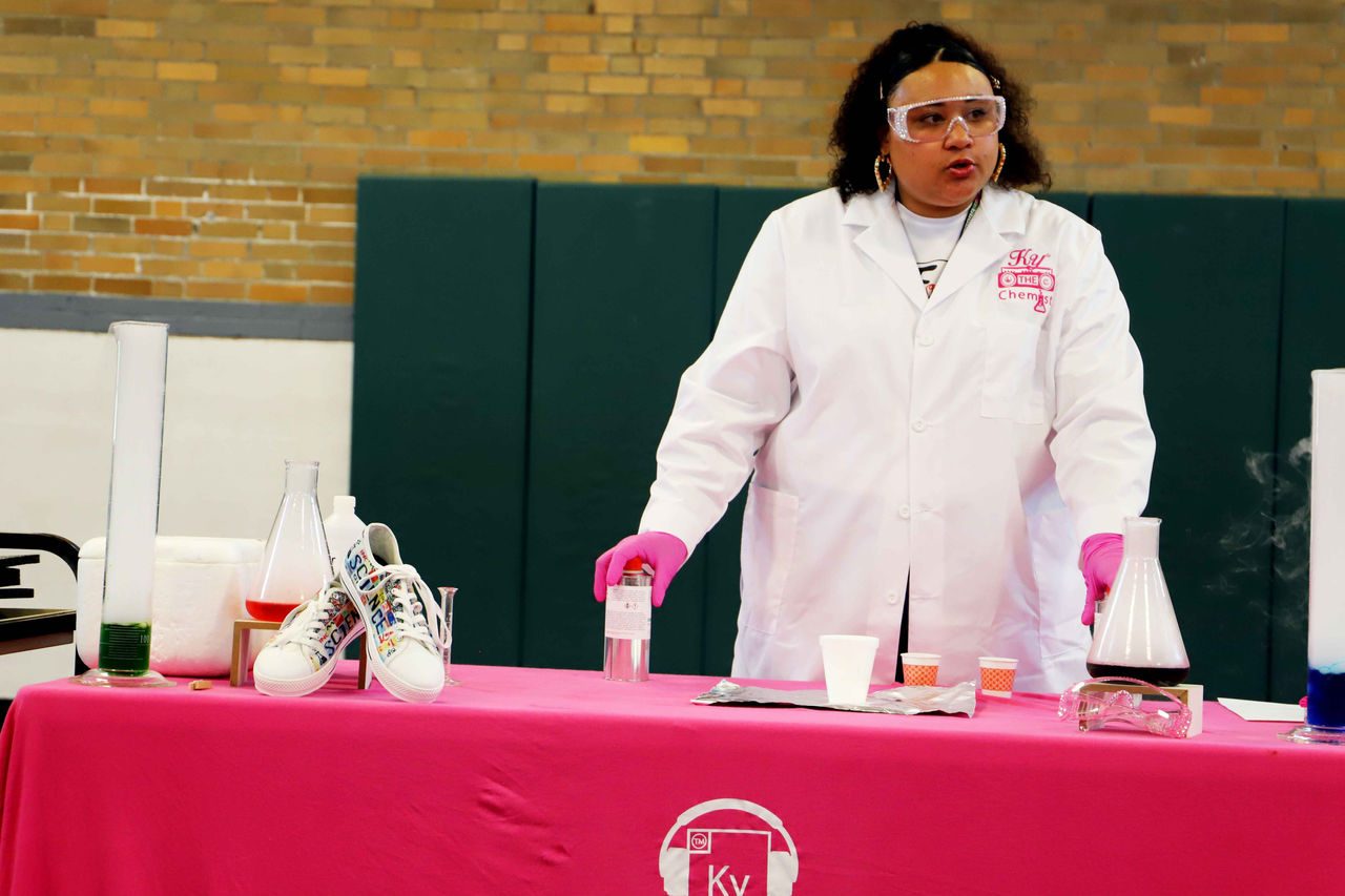 Jakyra Simspson at chemistry display table giving instructions during STEAM Sneakerheadz workshop.